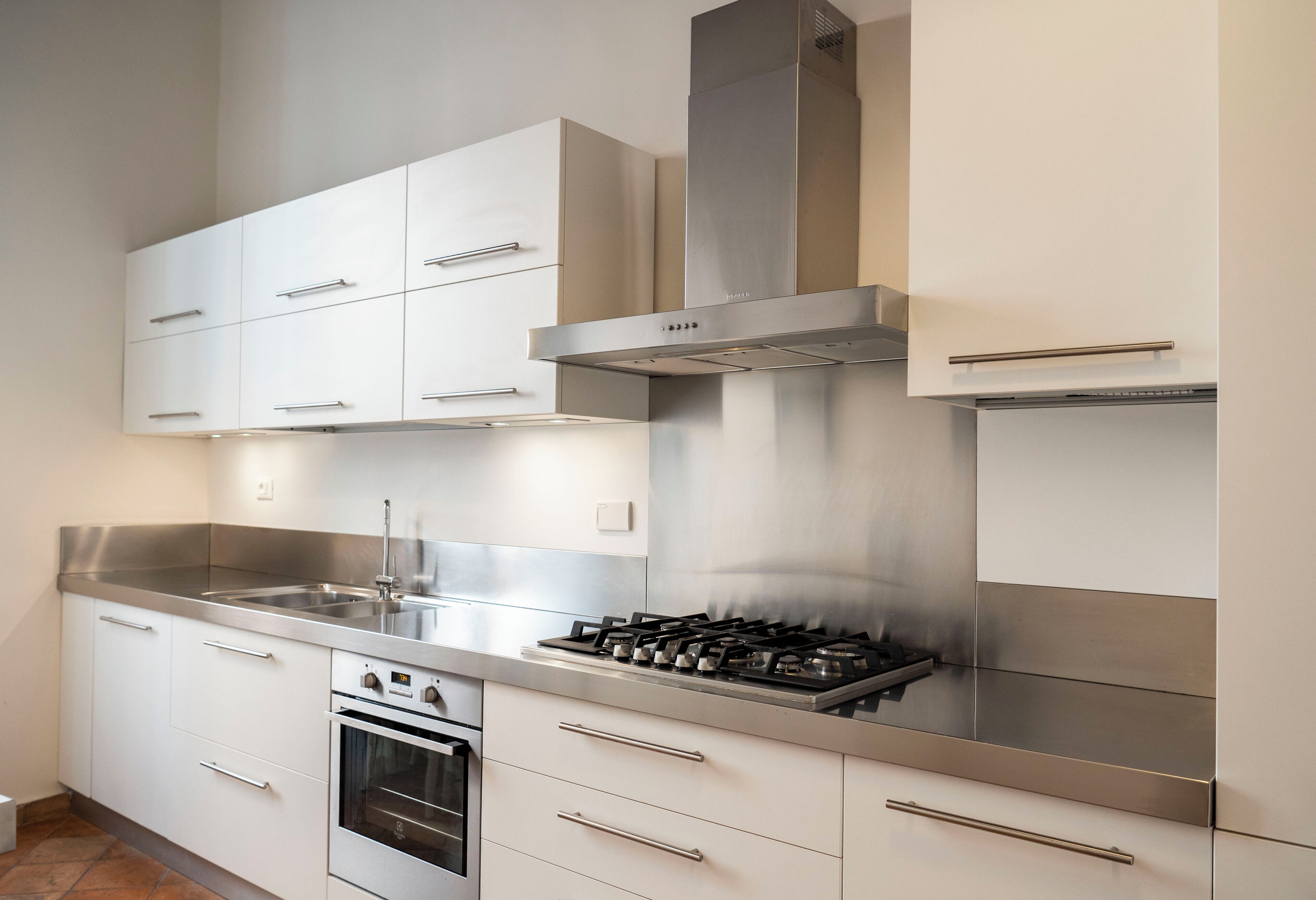 A modern kitchen with stainless steel appliances, white cabinetry, and a built-in oven.