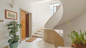 Un intérieur moderne avec un escalier en marbre, une porte en bois, un tableau encadré au mur et des plantes en pot.