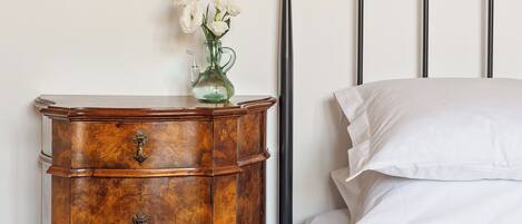 Un dormitorio con una cama, una mesita de noche con un florero y una lámpara de pared.