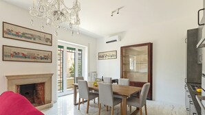 Un coin repas avec une table en bois, des chaises grises, un lustre et une cheminée.