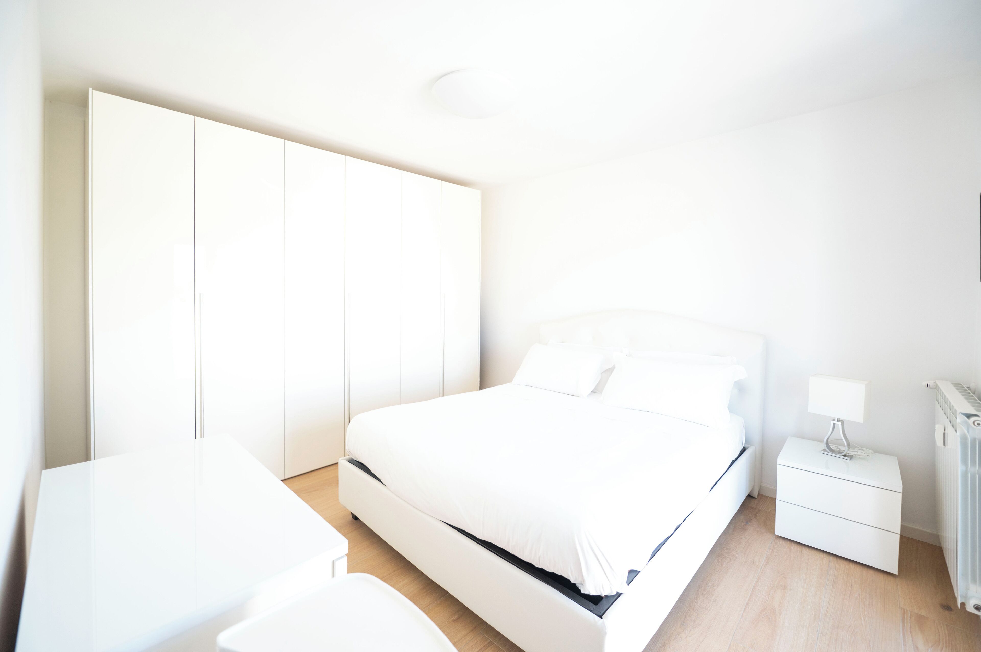 Un dormitorio moderno y minimalista con una cama grande, una mesita de noche y un armario.