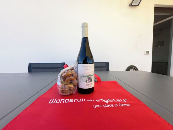 A table with a bottle of wine, a bag of snacks, and a red placemat with text. - Caffarella Park Terraced 2Br Apartment (Rome)