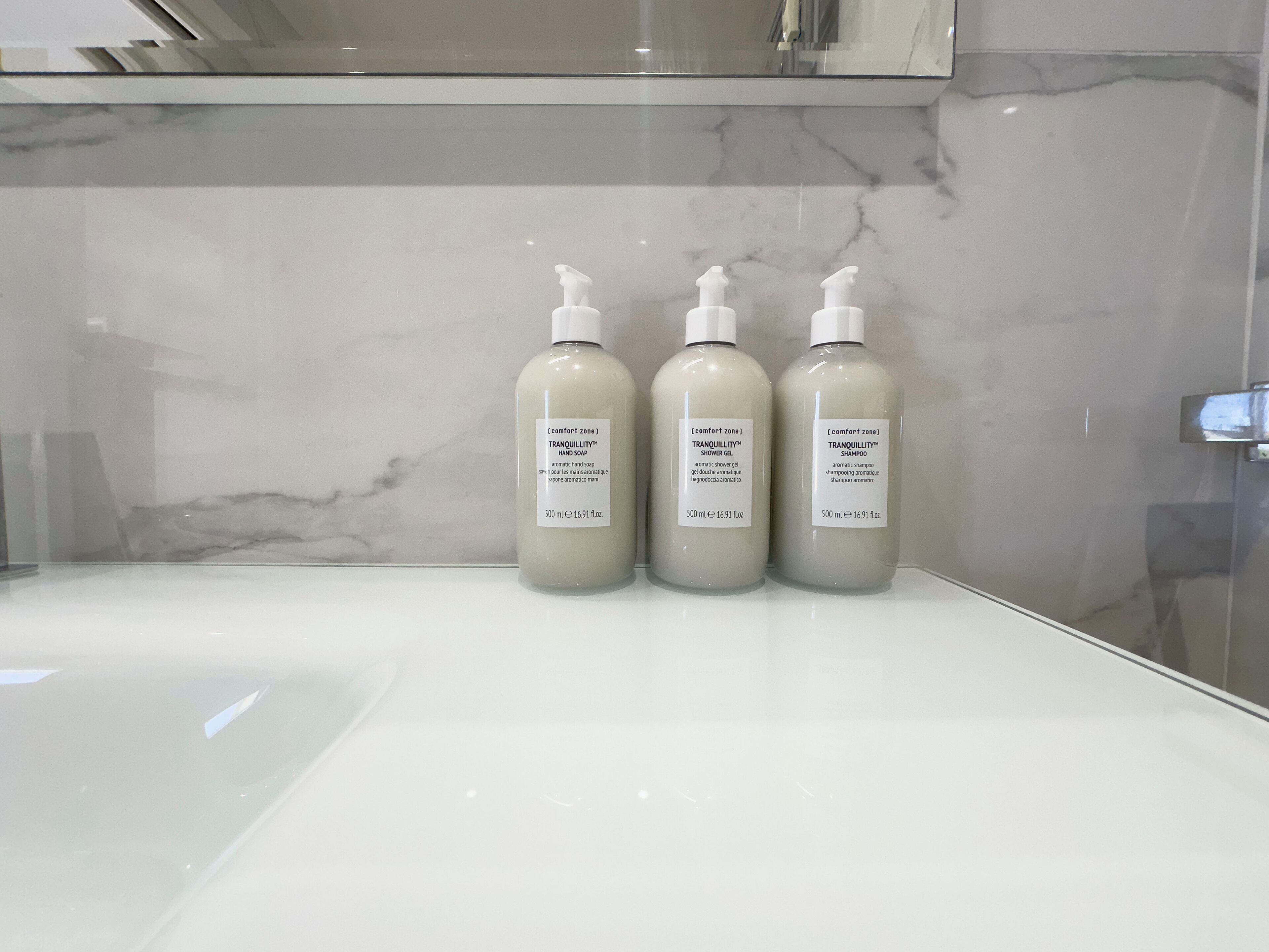 Drei Flaschen beruhigende Handseife, Duschgel und Shampoo auf einer weißen Waschtischplatte.