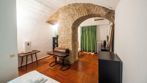 Ein Zimmer mit einem steinernen Bogen, einem Heizkörper, einem grünen Vorhang, einem Tisch mit einer Bank und einem weißen Schrank.