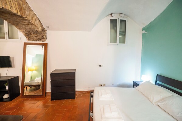 A bedroom with a bed, a dresser, a mirror, a TV, and a window.
