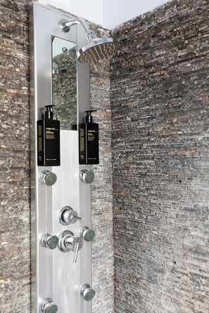 Une salle de bain moderne avec une douche verticale, un grand miroir et deux flacons d’huile d’argan.