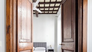 Een gang die leidt naar een slaapkamer met een bed, nachtkastje en plafondventilator.