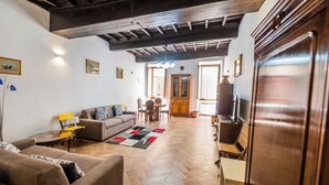A spacious living room with a herringbone floor, a sofa, a coffee table, and a dining area with chairs and a table. - Campo De Fiori Large Family Apartment (Rome)
