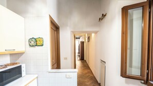 A narrow hallway with a kitchen area on the left, featuring a microwave and a stove. The hallway has wooden flooring and white walls. - Campo De Fiori Large Family Apartment (Rome)