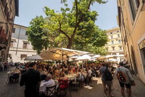 Ein lebhaftes Straßencafé mit Tischen und Sonnenschirmen, umgeben von Gebäuden.