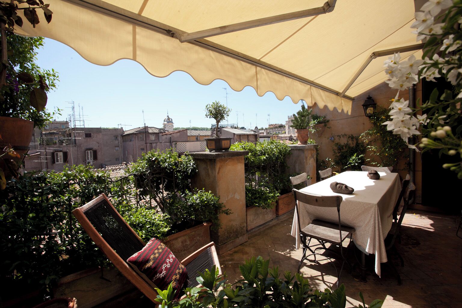 Un espacio de estar al aire libre cubierto con una mesa y sillas, rodeado de plantas en macetas y vistas panorámicas de la ciudad.