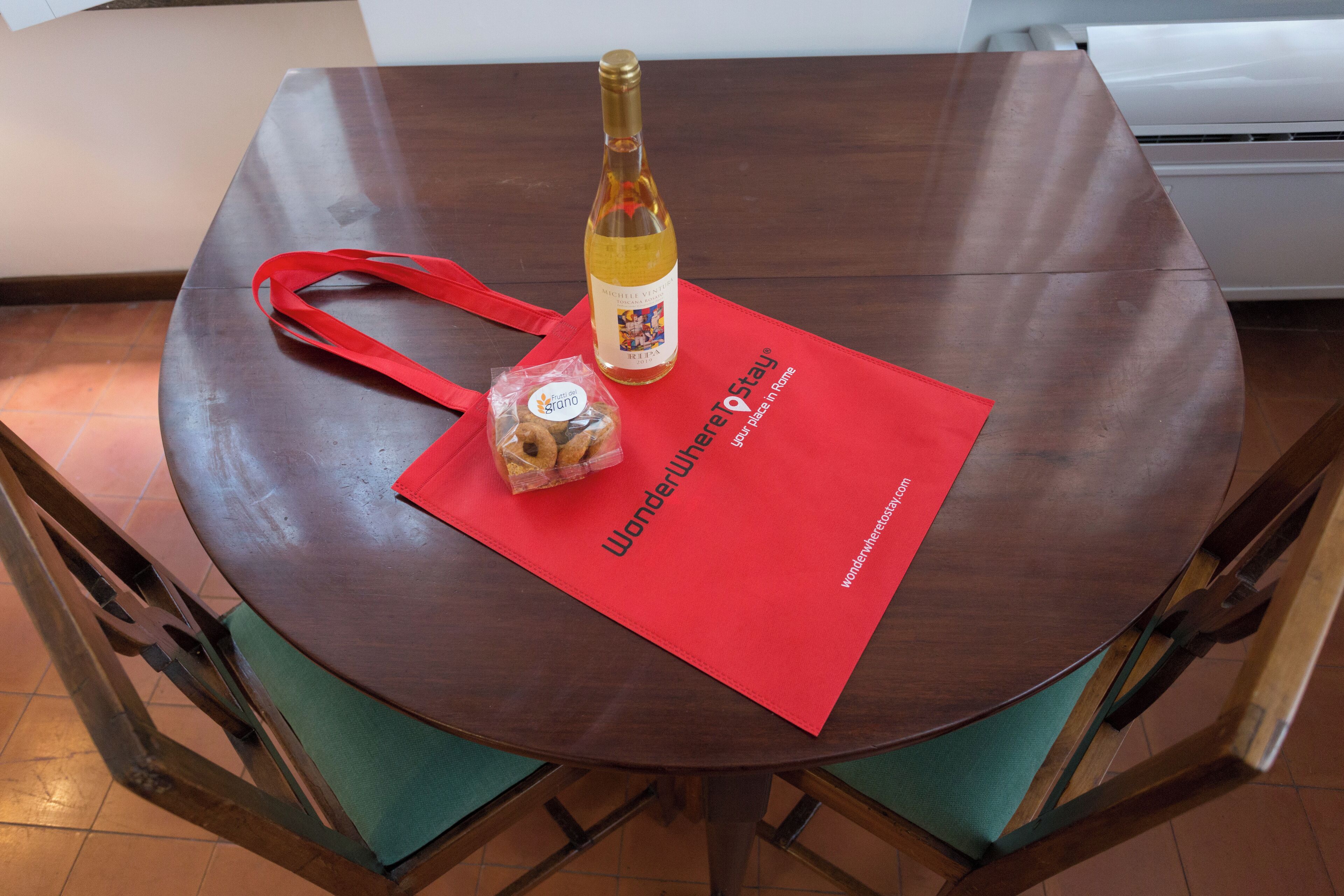 Una mesa de madera redonda con un posavasos rojo, una botella de vino y un objeto pequeño envuelto.