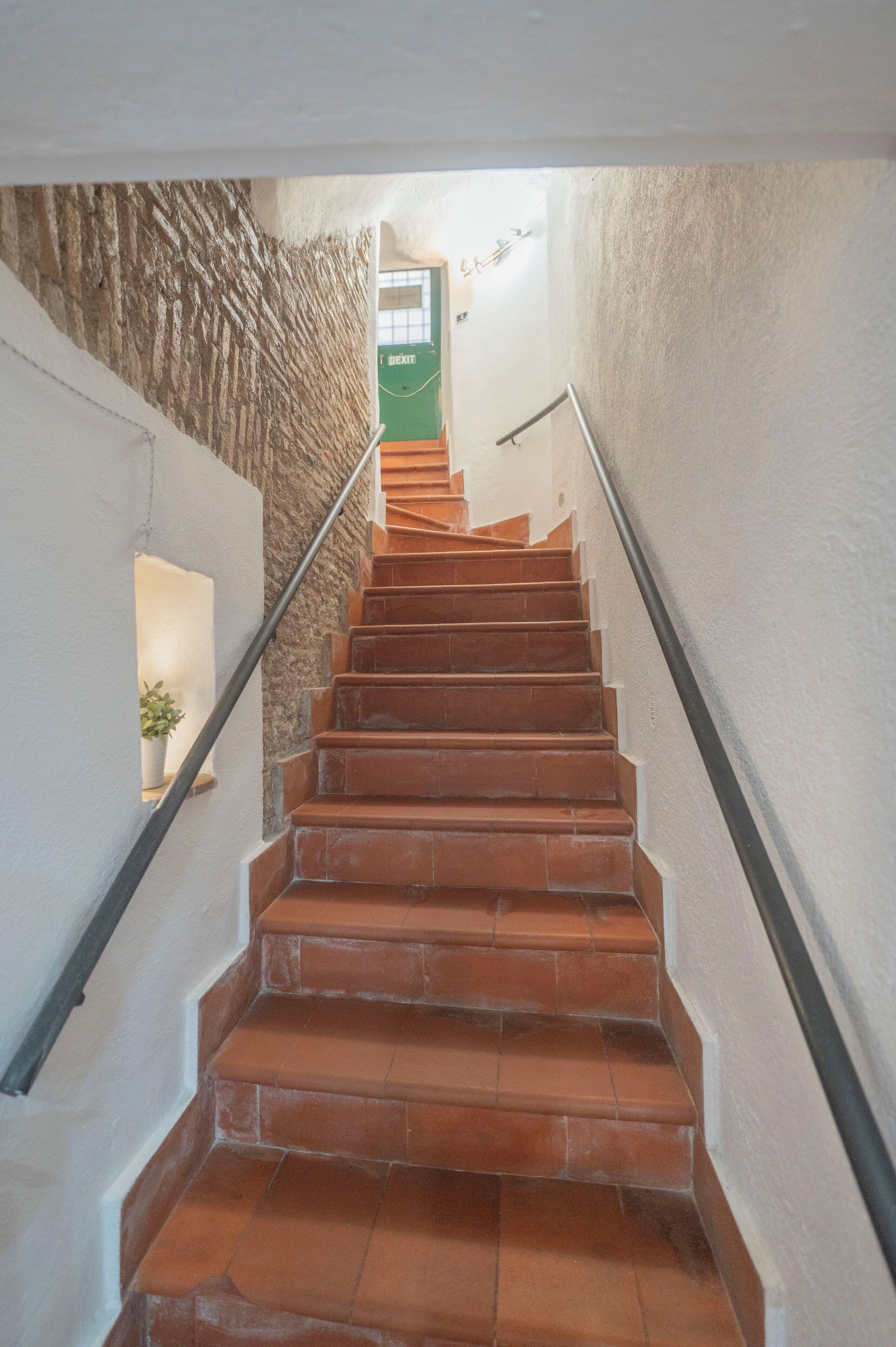 A staircase with terracotta steps, white walls, and a green door at the top.
