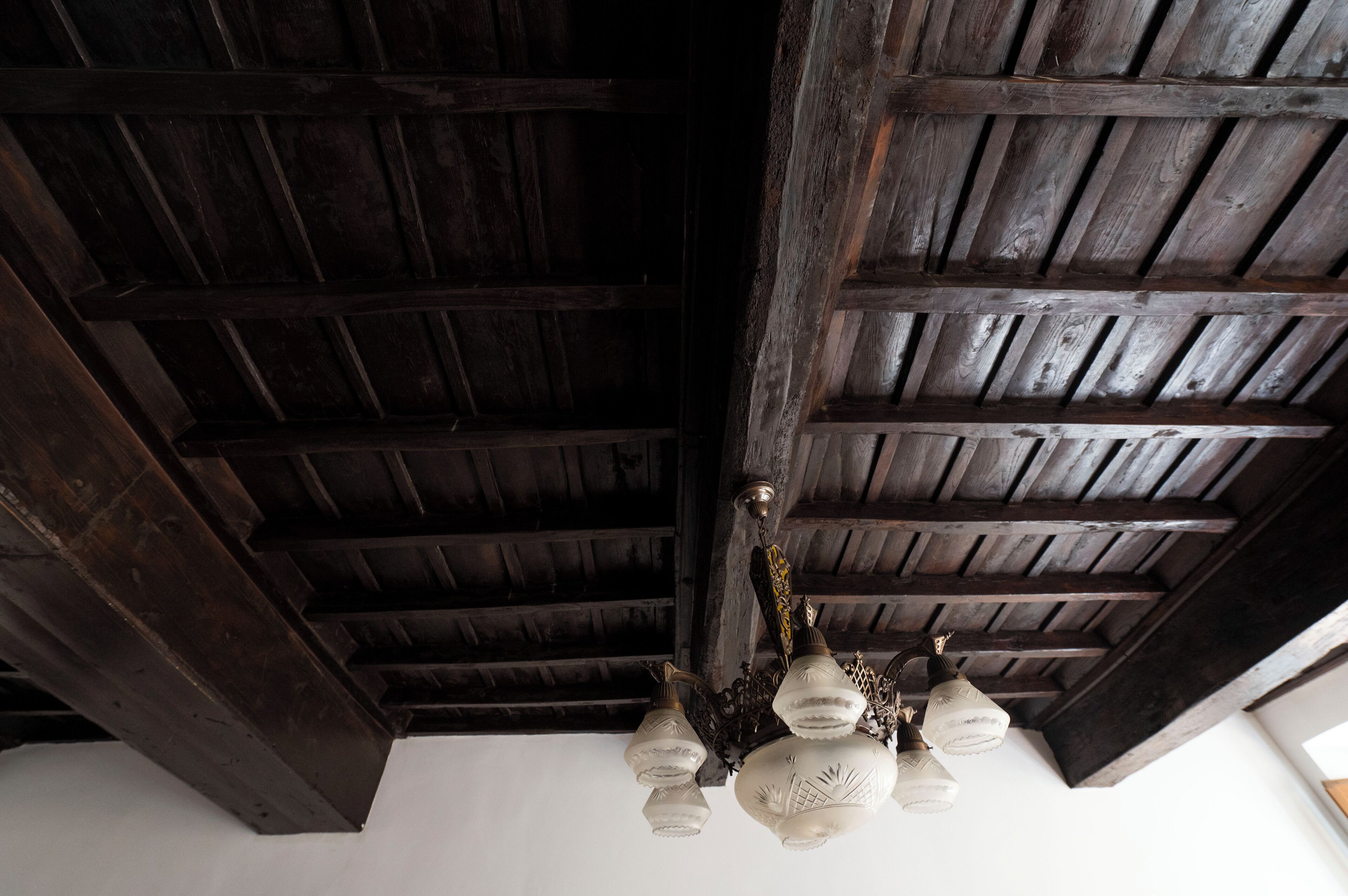 Teto com vigas de madeira escura e um lustre com várias cúpulas de vidro.