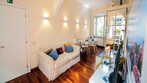 A cozy room with a white sofa, wooden flooring, a dining area with a table and chairs, and a large window offering a view of the outdoors. - Colosseum 2Br Elegance And Charm  (Rome)