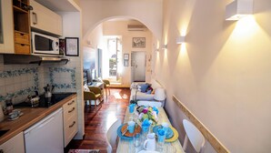 A compact kitchen with a microwave, stove, and wooden cabinets. A dining area with a table set for two is visible, featuring blue and white tableware. - Colosseum 2Br Elegance And Charm  (Rome)