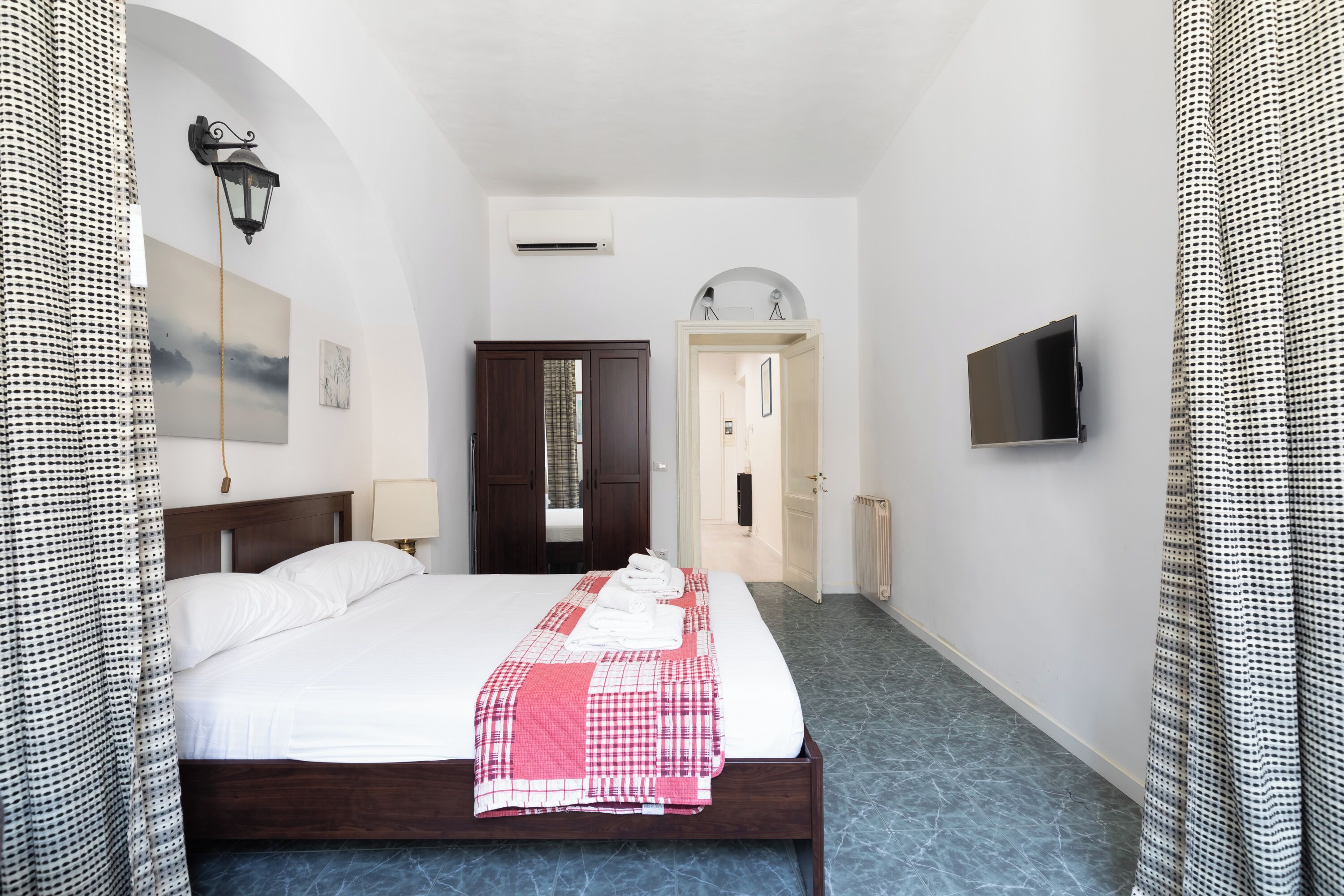 A hotel room with a large bed, a TV, a wardrobe, and a door leading to another room.