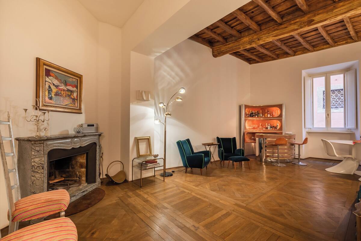 A living room with a fireplace, wooden flooring, a painting, and a bar area.