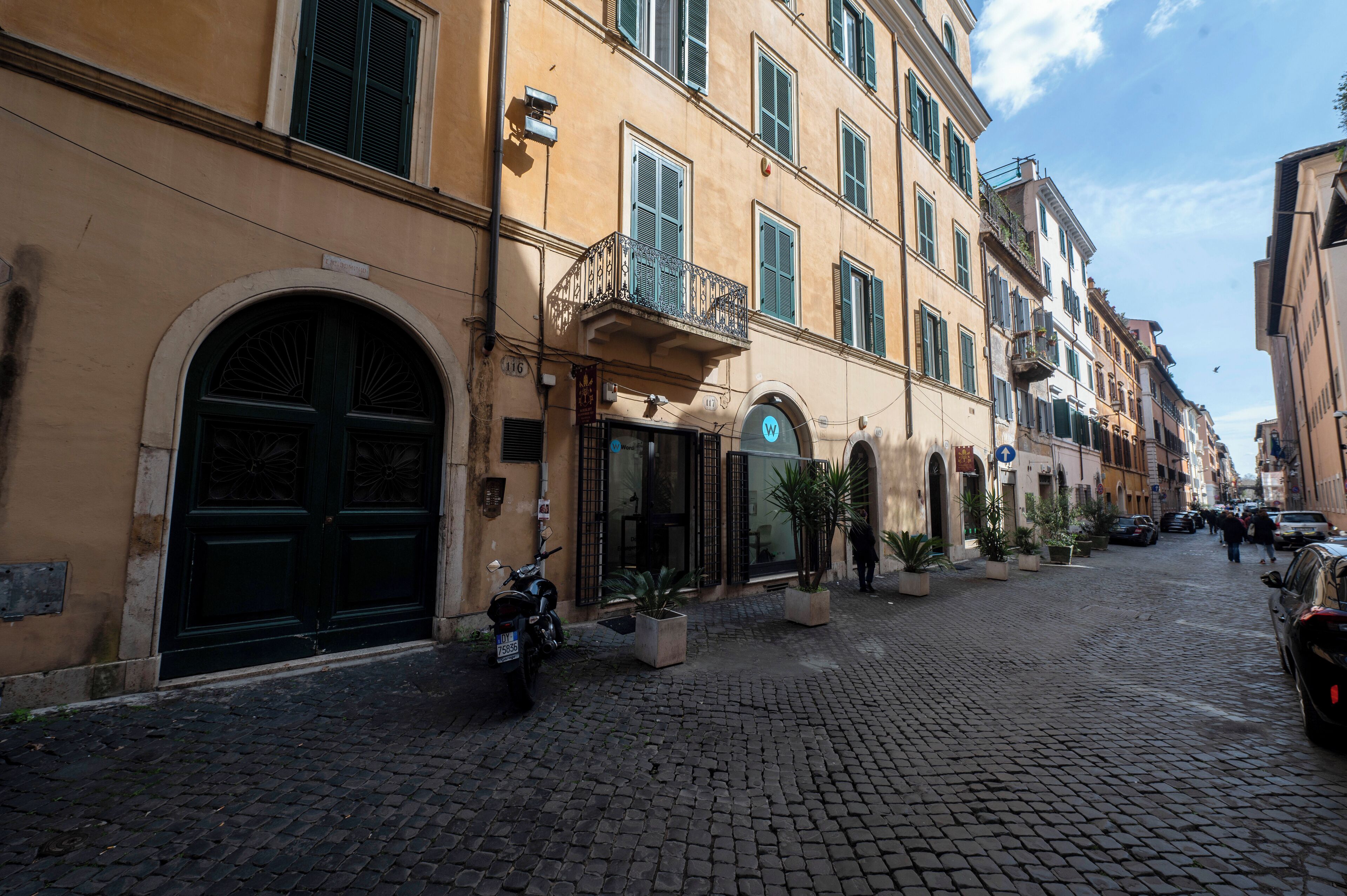 Una calle empedrada flanqueada por edificios históricos, una motocicleta estacionada y macetas con plantas.