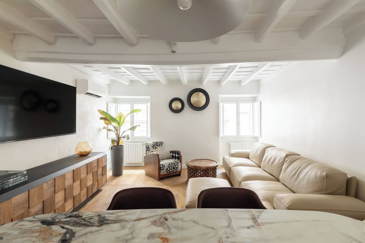 A modern living room with a marble table, a sofa, a TV mounted on the wall, and a potted plant.
