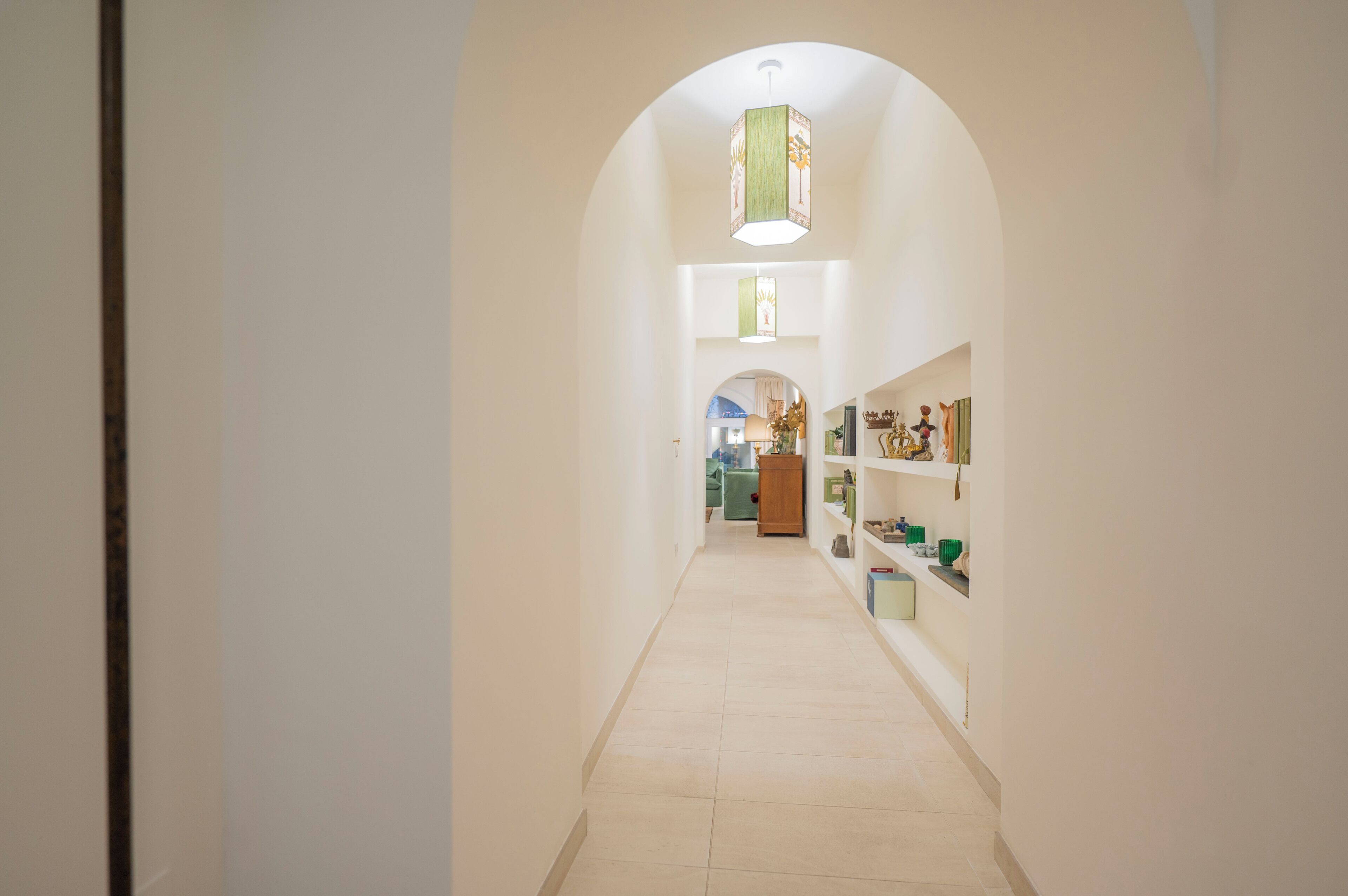 A hallway with an arched ceiling, a wooden cabinet, and shelves with various items.