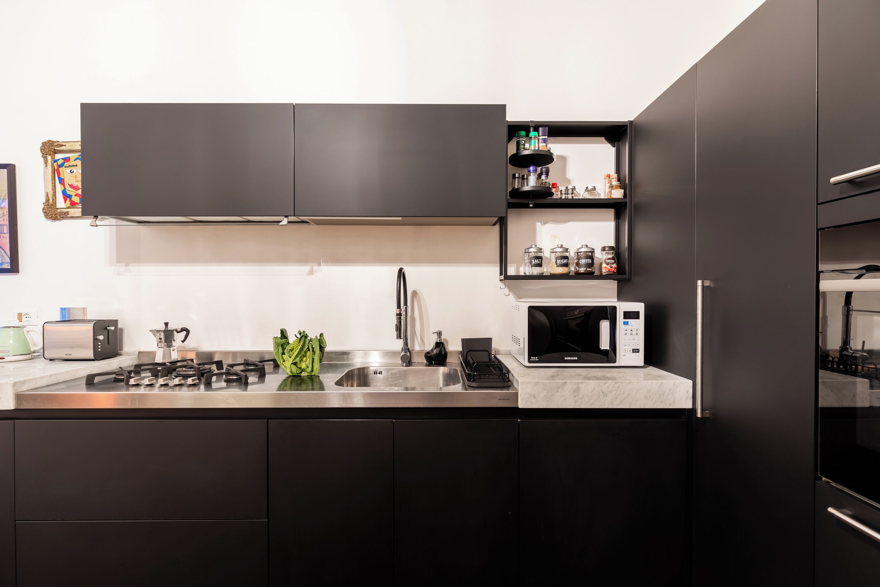 Une cuisine moderne avec des meubles de couleur sombre, un évier en acier inoxydable, un four à micro-ondes et une cuisinière à gaz.