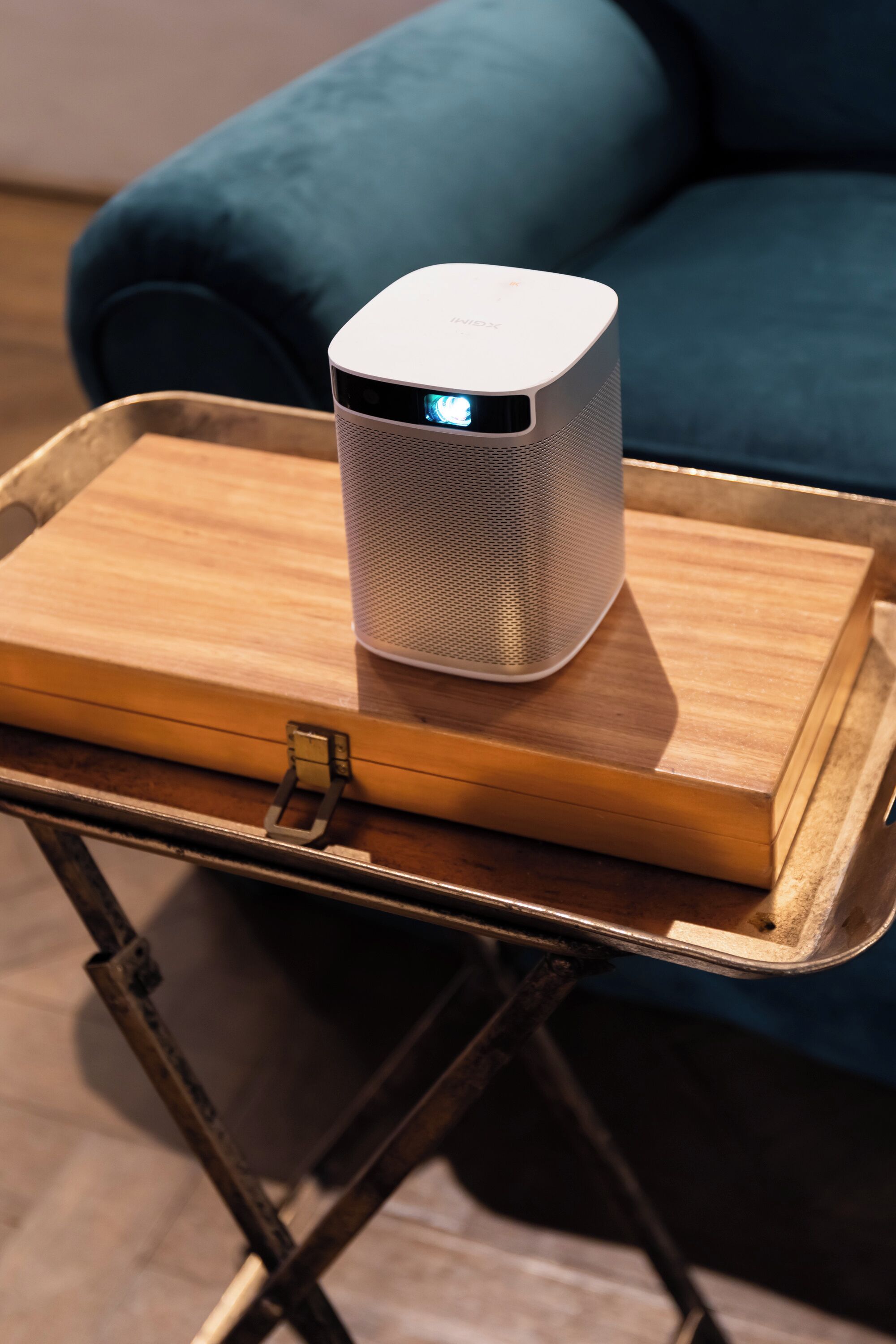 A white portable speaker on a wooden tray placed on a metal stand.