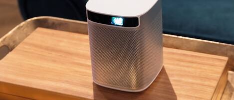 A white portable speaker on a wooden tray placed on a metal stand.