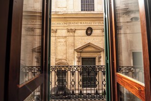 A view through a window with ornate iron railings, a stone building facade, and a door with a circular emblem. - Via Giulia Apartments (Rome)