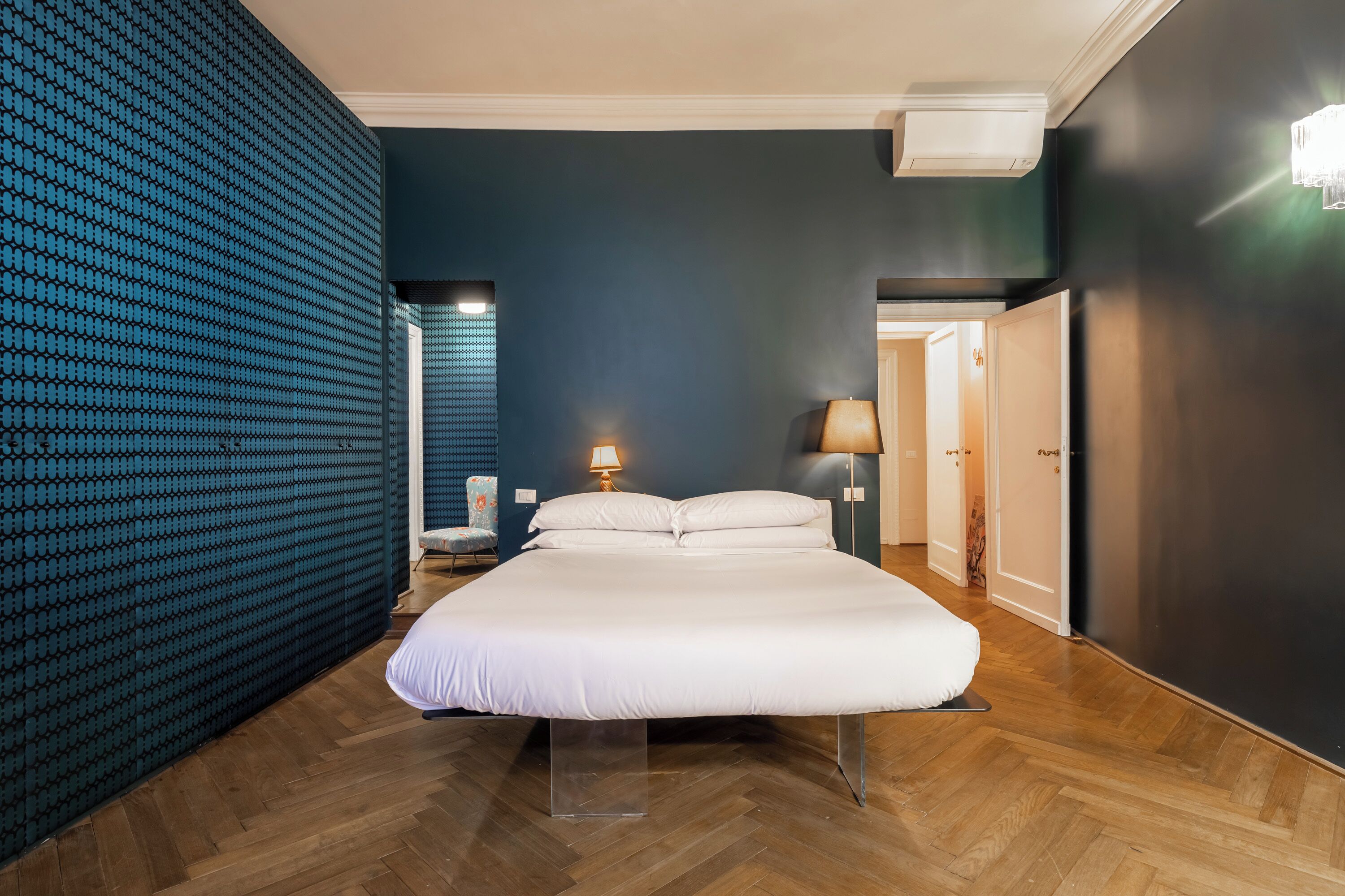 A modern hotel room with a large bed, a patterned wall, and a wooden floor.