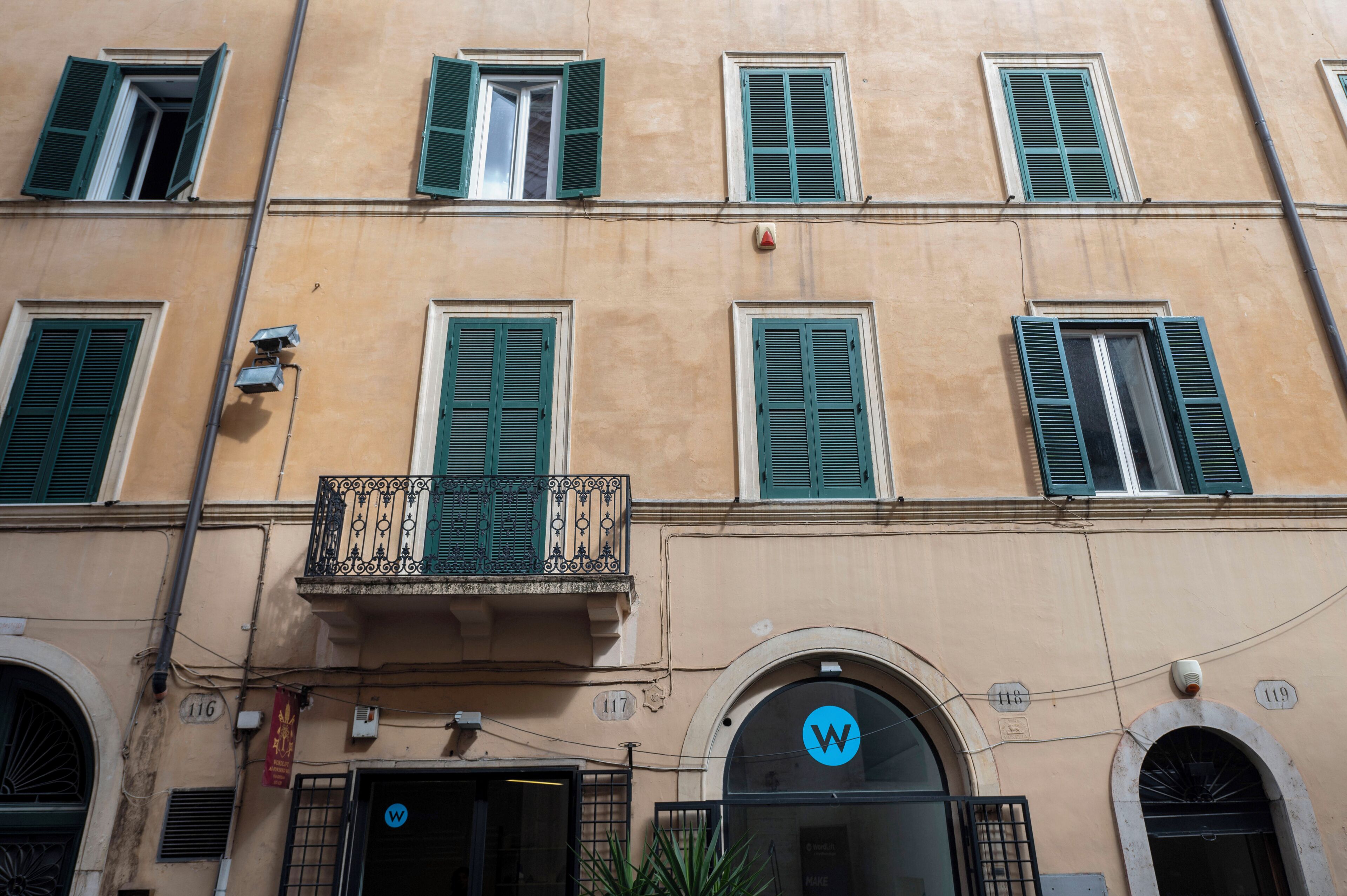 Un bâtiment doté de nombreuses fenêtres, dont certaines sont équipées de volets, et d’une porte ornée d’un logo « W » bleu.
