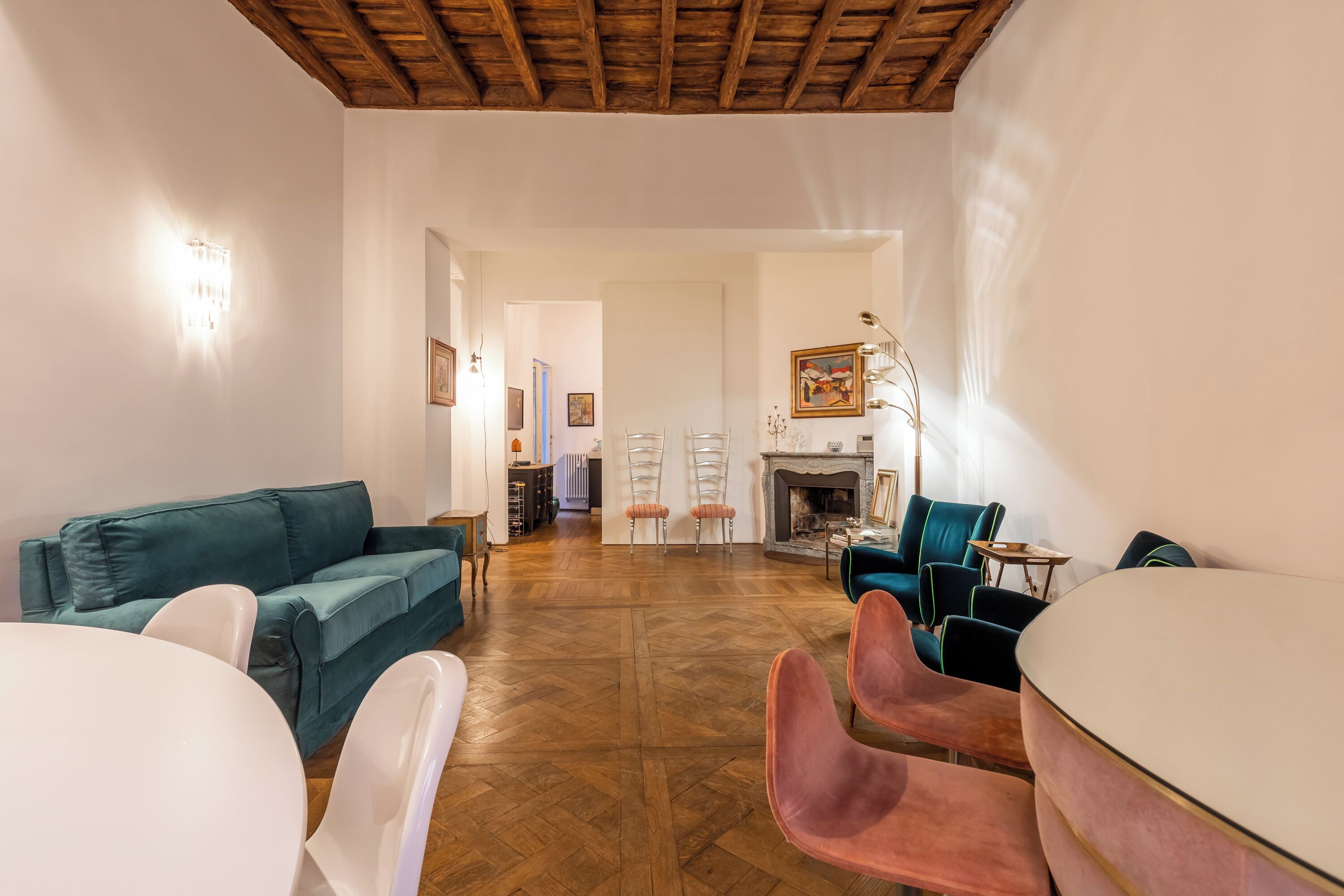 A spacious living room with a wooden ceiling, a green sofa, a white table, and pink chairs.