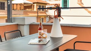Una terraza en la azotea con una mesa, sillas, una botella de vino y un jarrón blanco.