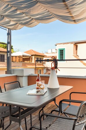 A rooftop terrace with a table, chairs, a bottle of wine, and a white vase. - Monteverde Apartments  (Rome)