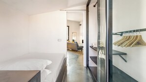 Une chambre d’hôtel moderne avec un lit, une cloison en verre et un portant à vêtements.