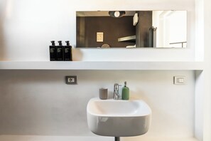 A modern bathroom with a white sink, a mirror above it, and three black bottles on the wall. - Monteverde Apartments  (Rome)