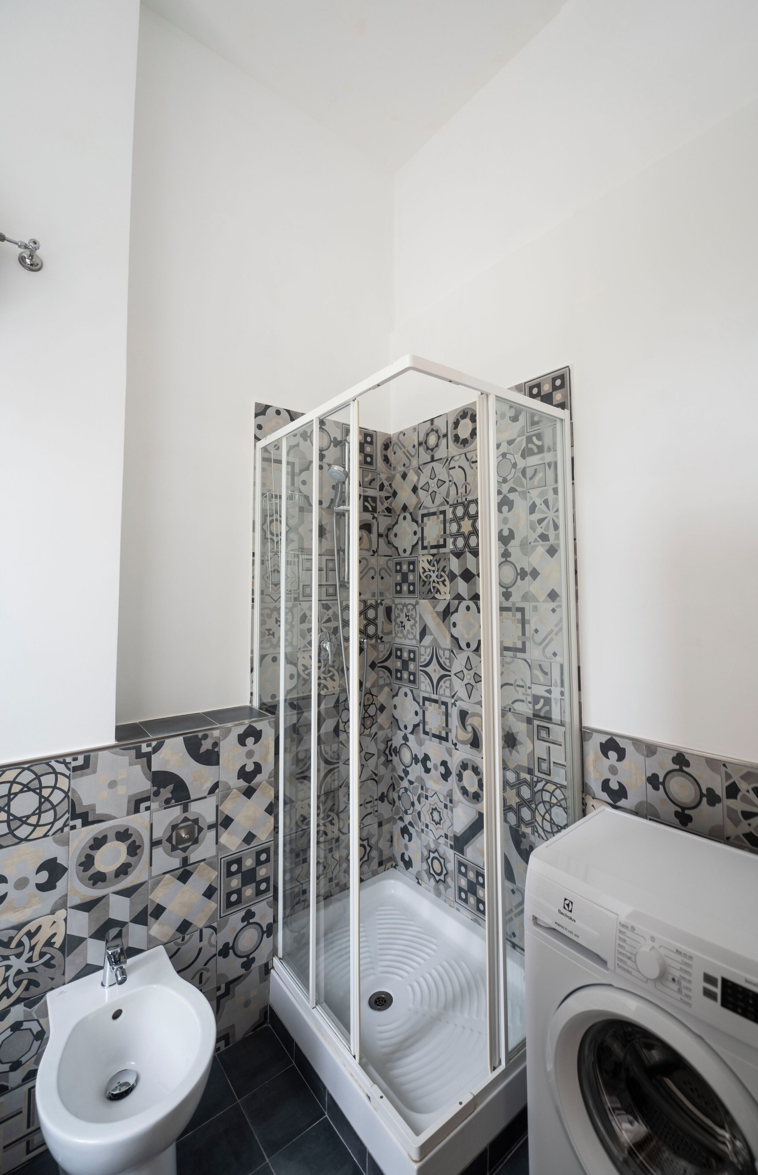A bathroom with a shower enclosure, a bidet, and a washing machine.