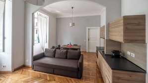 A modern living room with a sofa, a dining table, and a kitchen area with wooden cabinets. - Lovely And New Apartment Near Termini Station  (Rome)