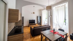 A modern living room with a sofa, dining table, and TV. There is a kitchen area with a sink and cabinets. - Lovely And New Apartment Near Termini Station  (Rome)