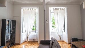 A modern living room with a sofa, a dining table, and a cabinet. There are two windows with curtains, and an air conditioning unit is visible. - Lovely And New Apartment Near Termini Station  (Rome)