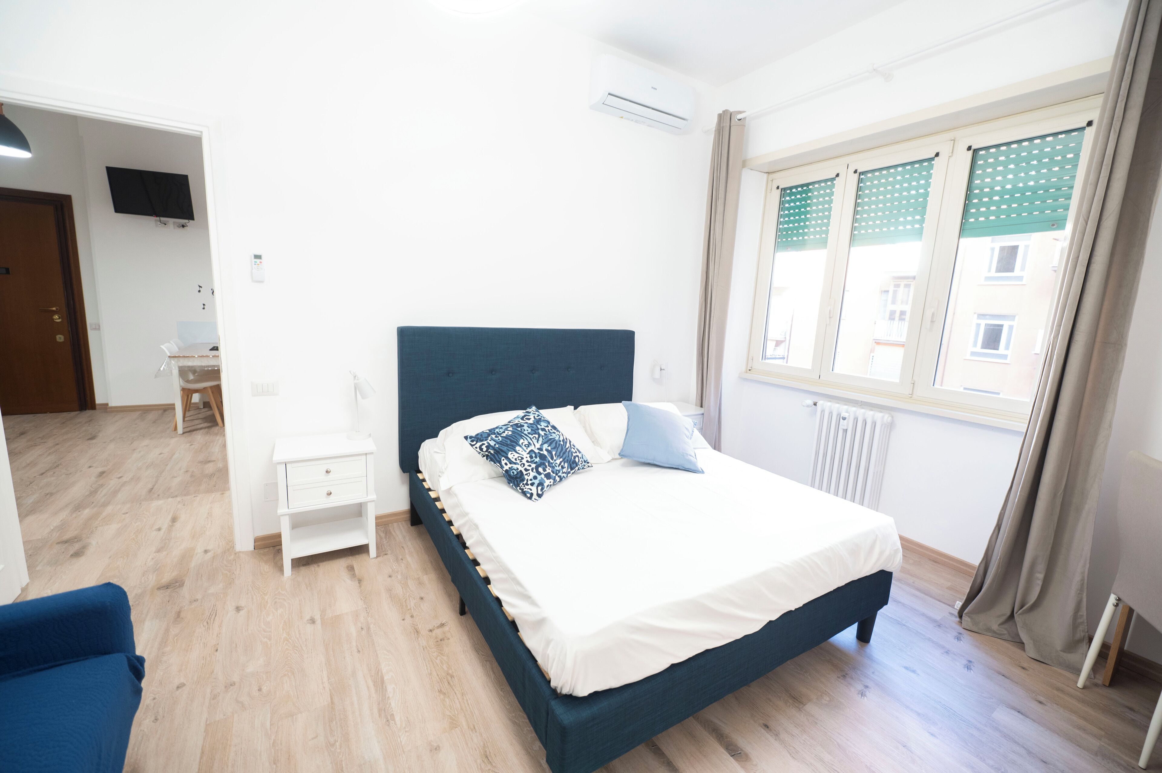 Une chambre à coucher comprenant un lit, une table de chevet, un téléviseur fixé au mur et une fenêtre avec des rideaux.