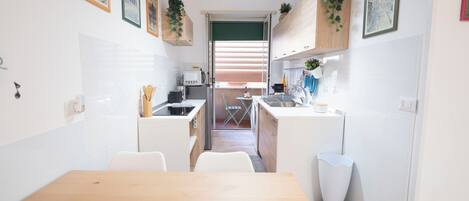 A compact kitchen with a dining table, white cabinets, and a view to the living area.