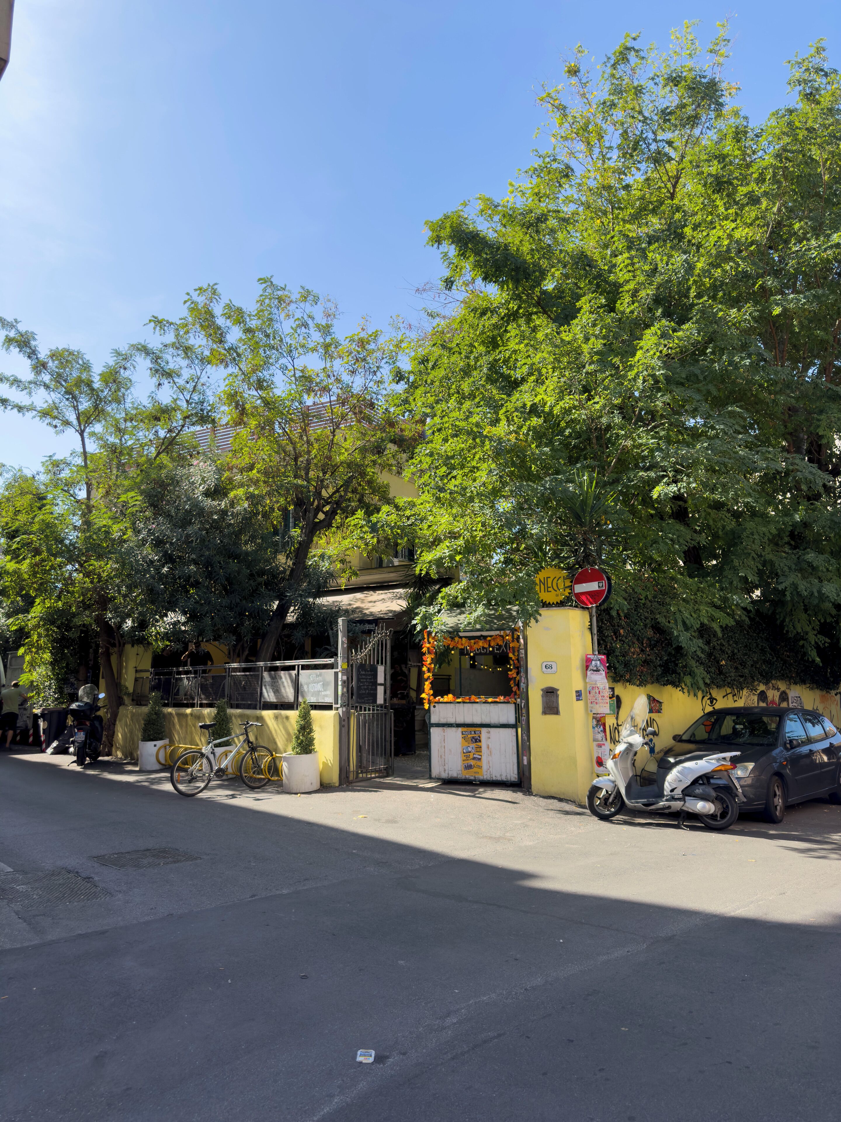 A street scene with a yellow building, a closed gate, a parked scooter, and a bicycle.