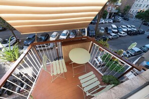 A balcony with a table and chairs, a hanging plant, and a view of parked cars and buildings. - Lovely Apartment In Hip And Vibrant Pigneto (Rome)