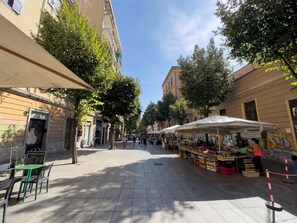A street with outdoor cafes, market stalls, and trees lining the sidewalk. - Lovely Apartment In Hip And Vibrant Pigneto (Rome)