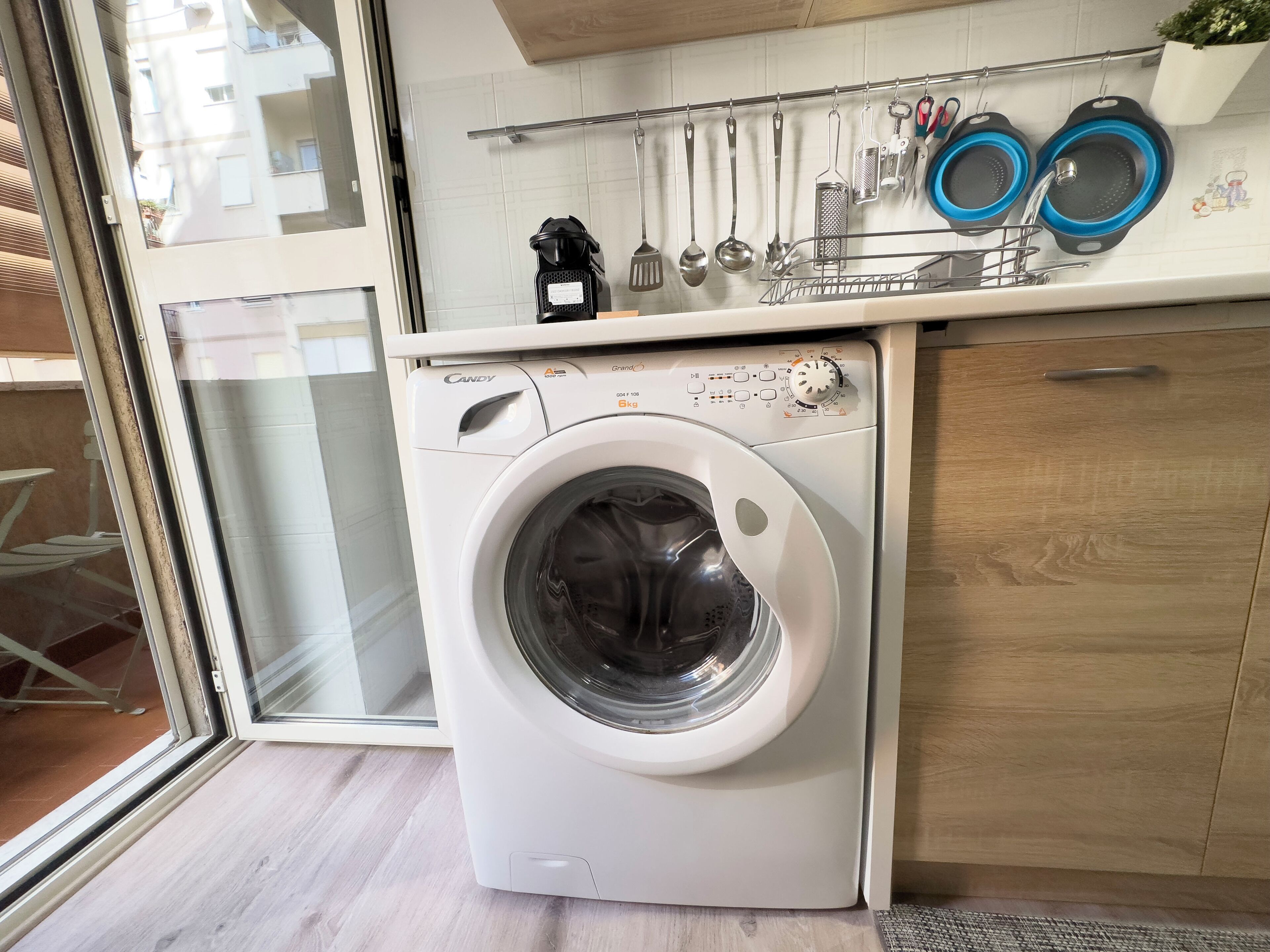 Een compacte, moderne keuken met een ingebouwde wasmachine, een droogrek en diverse keukengerei.