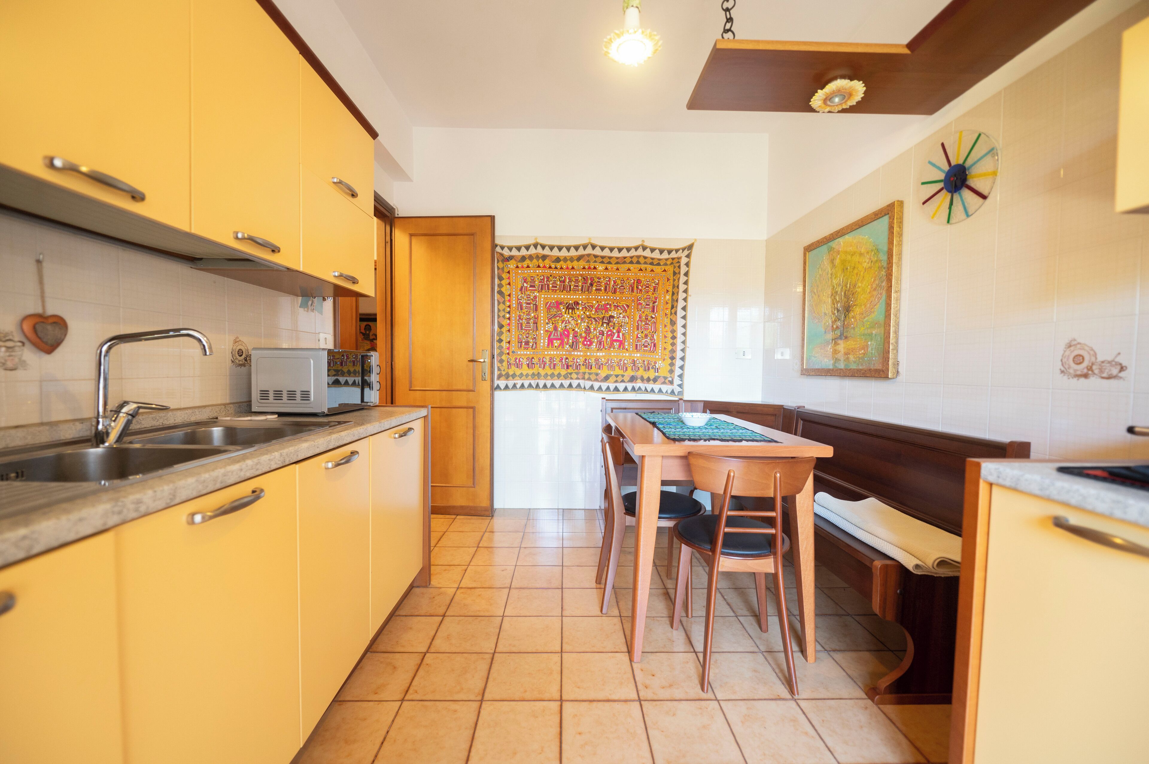 A compact kitchen with yellow cabinets, a microwave, a sink, and a dining table with chairs.