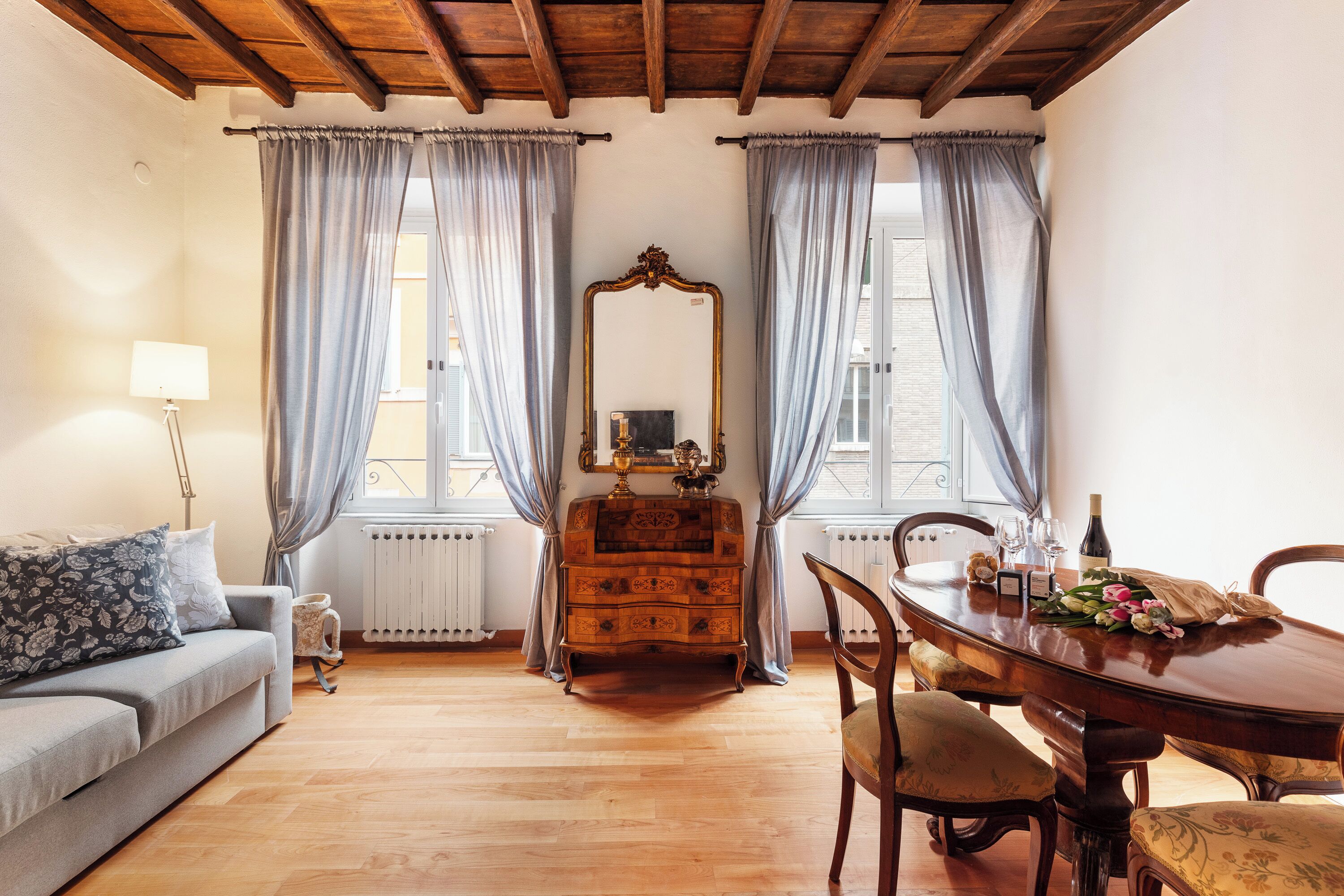Una stanza con soffitto in legno, un divano, una cassettiera, un tavolo con sedie e uno specchio.