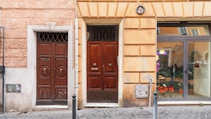 A building facade with two wooden doors, a window with a glass display, and a cobblestone street. - Monti  Apartments (Rome)