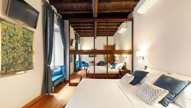 A hotel room with a large bed, a TV mounted on the wall, and a wooden ceiling. - Monti  Apartments (Rome)